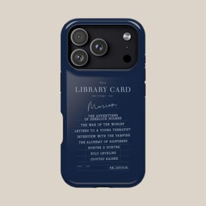 May include: A navy blue phone case featuring a library card design. The text reads "This Library Card belongs to: Mariam" with a list of book titles. The case has a camera cutout and a sleek, modern design.