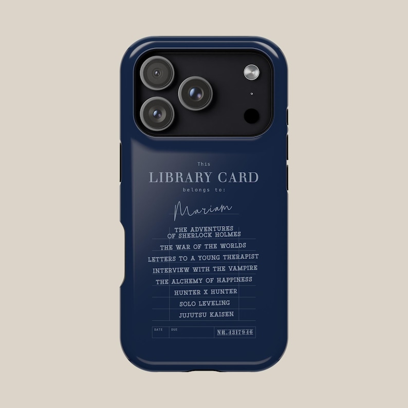 May include: A navy blue phone case featuring a library card design. The text reads "This Library Card belongs to: Mariam" with a list of book titles. The case has a camera cutout and a sleek, modern design.