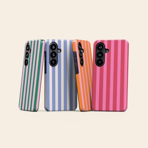 Op de afbeelding: Vier smartphonehoesjes die rechtop staan, elk met een verticaal streeppatroon. De hoesjes tonen kleurcombinaties van groen en roze, lichtblauw en wit, oranje en roze, en twee tinten roze, allemaal voorzien van zwarte uitsparingen voor de camera.