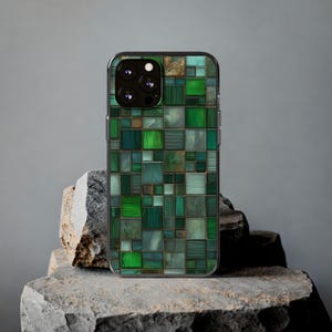 Op de afbeelding: Een smartphonehoesje met een mozaïekpatroon in groen, blauwgroen en goudtinten. Het ontwerp bestaat uit onregelmatige vierkanten en rechthoeken, wat een textuur geeft. De cameralenzen van de telefoon zijn zichtbaar aan de bovenkant.