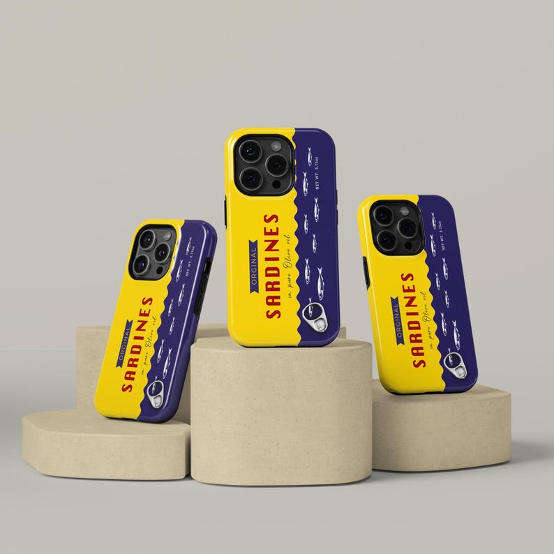 May include: Yellow and navy blue phone cases with a sardine can design. The cases feature the text "ORIGINAL SARDINES in pure olive oil" and a graphic of sardines. The cases are displayed on beige pedestals.