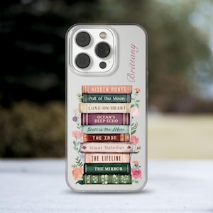 May include: Clear phone case featuring a stack of books with titles like "Hidden Roots" and "The Mirror." Floral accents and the name "Brittany" are printed on the case. The case is designed for a smartphone.