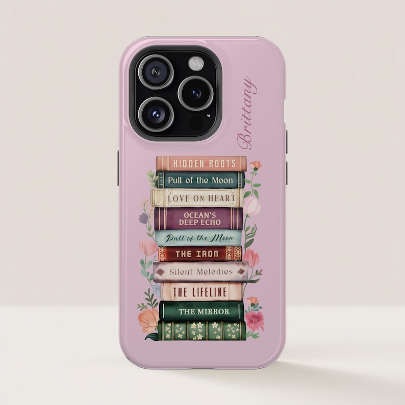 K&ouml;nnte beinhalten: Rosa Handyh&uuml;lle mit einem Stapel B&uuml;cher, darunter Titel wie "Hidden Roots" und "Love on Heart". Blumenmuster und der Name "Brittany" sind ebenfalls zu sehen. F&uuml;r ein Smartphone.