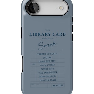 May include: A blue phone case featuring a library card design. The text reads "This LIBRARY CARD belongs to: Sarah." Below are book titles like "Throne of Glass" and "Crescent City." The case has a camera cutout.