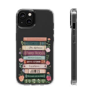 May include: Clear phone case featuring a stack of books with titles like "Good Girl" and "Funny Story." Floral accents and the text "JAMES" are visible. The case is designed for a smartphone.