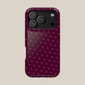 May include: A burgundy phone case with a repeating pattern of small, light pink polka dots. The case has a glossy finish and features a camera module with three lenses and a flash.