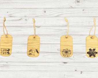 May include: Four wooden gift tags with different Christmas designs. The tags are brown and have a string attached to the top. The designs include a gift box, a reindeer, a snowflake, and a pinwheel.
