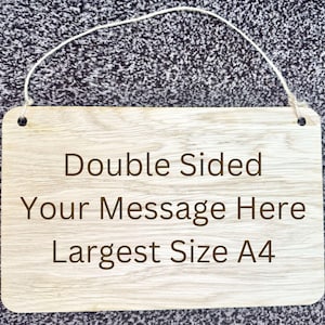 Può includere: Un cartello di legno con una corda bianca per appenderlo. Il cartello è a doppia faccia e dice "Double Sided Your Message Here Largest Size A4".