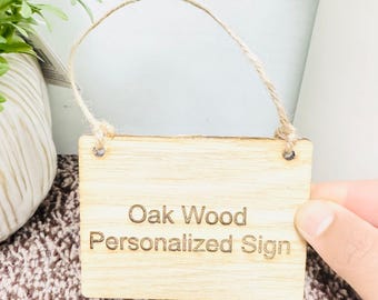 May include: A natural wood sign with a twine hanger. The sign is engraved with the text "Oak Wood Personalized Sign".