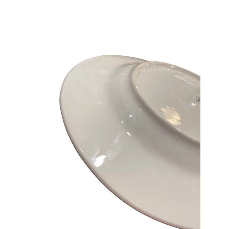 May include: A white ceramic plate with a glossy finish. The plate has a slightly curved rim and a shallow center. The underside of the plate is visible, showing a smooth, clean surface.