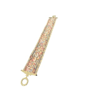 May include: A long, rectangular fabric bell pull featuring a detailed tapestry pattern of colorful fruits, flowers, and leaves. The textile is secured at both ends by ornate, polished gold-tone metal hardware, each featuring a circular hanging ring.