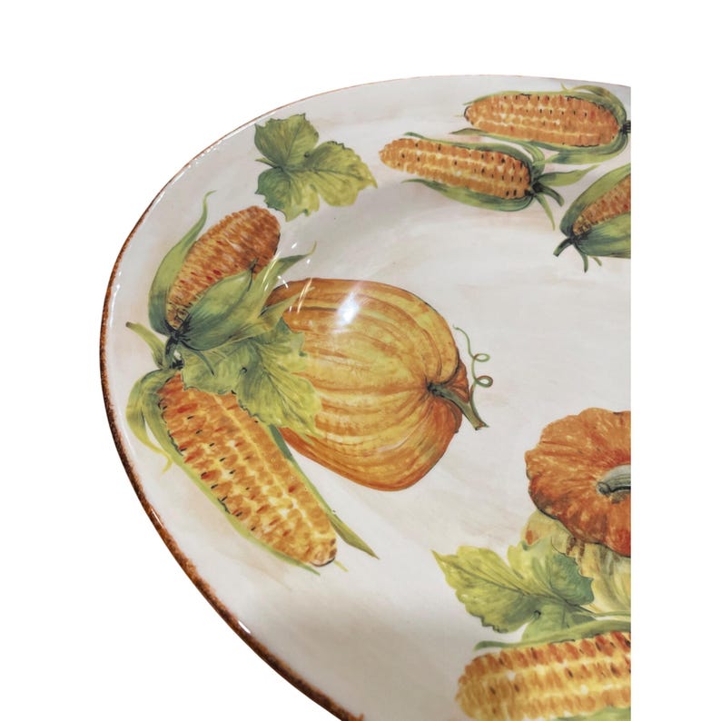 May include: A white ceramic serving platter with a hand-painted harvest design. The design features pumpkins, corn on the cob, and green leaves. The rim of the platter has a brown border.