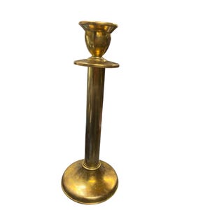 May include: A vintage brass candlestick holder with a round base, a long, slender stem, and a cup-shaped top. The candlestick is made of shiny, polished brass and is designed to hold a single candle. The overall design is simple and elegant.