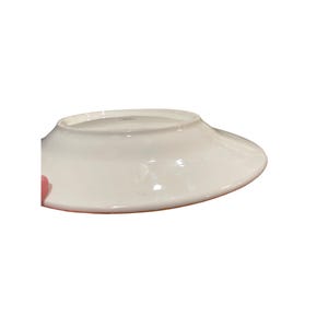 May include: A white ceramic plate with a wide, slightly curved rim. The plate is glossy and appears to be clean. The underside of the plate is visible, showing the rim's shape and the plate's overall design. The plate is likely for serving food.