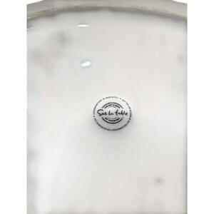 May include: A white ceramic serving dish with a rounded edge. The center features a circular emblem with the text "Sur la table of cooking". The dish is marked "Made in Italy".