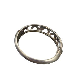 May include: A silver-toned bangle bracelet with an openwork design. The bracelet features a series of arched cutouts along the top edge, creating a decorative pattern. The metal has a polished finish, reflecting light.