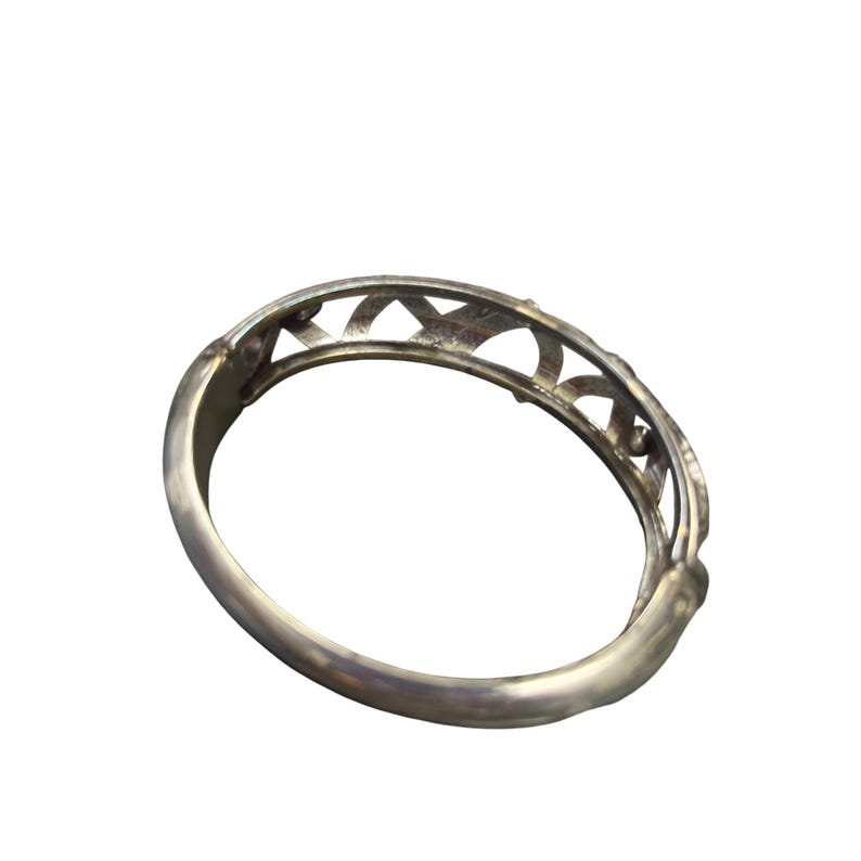 May include: A silver-toned bangle bracelet with an openwork design. The bracelet features a series of arched cutouts along the top edge, creating a decorative pattern. The metal has a polished finish, reflecting light.