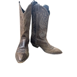 May include: A pair of brown leather cowboy boots with decorative stitching. The boots have pointed toes and a worn, distressed appearance. The boots are a classic Western style, often seen in the UK.
