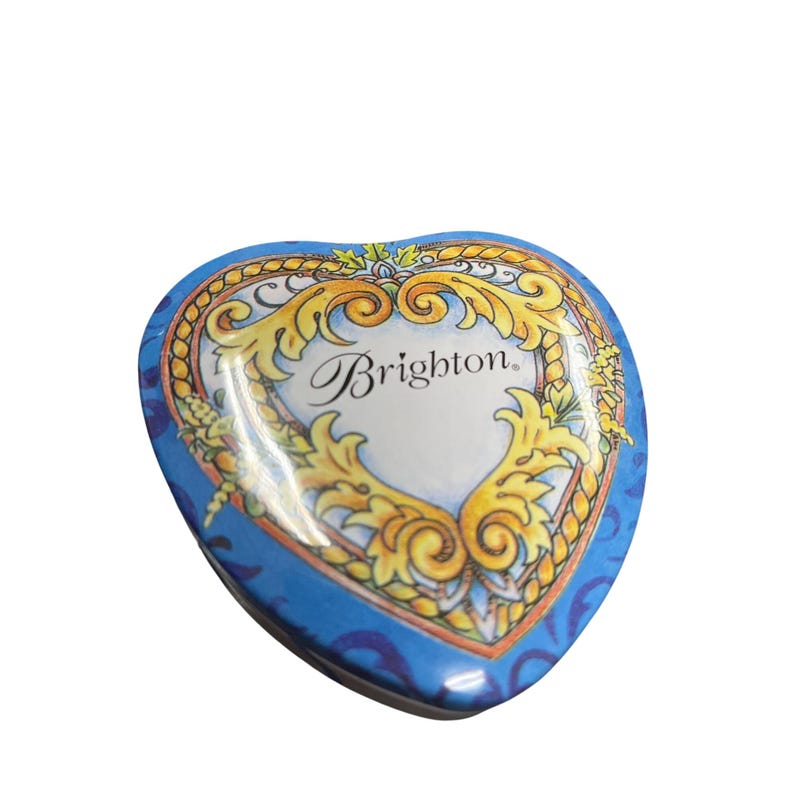 May include: A heart-shaped blue tin with a decorative gold and yellow design. The tin features the word "Brighton" in elegant script on a white background. The tin is a collectible item.