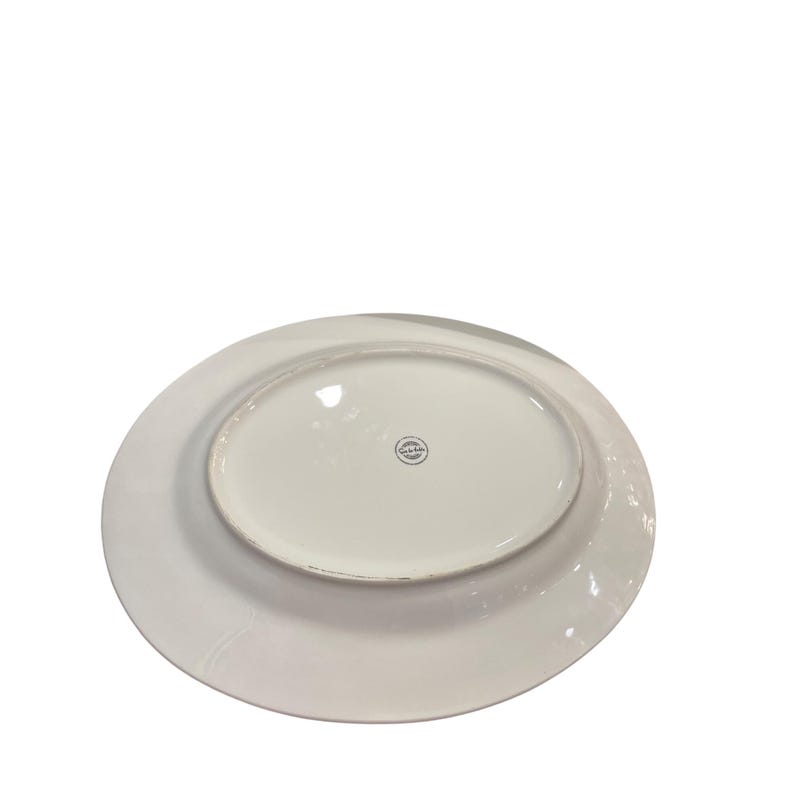 May include: White oval serving platter with a slightly raised rim. The underside of the platter is visible, showing a central oval area and a circular logo. The platter is made of ceramic.