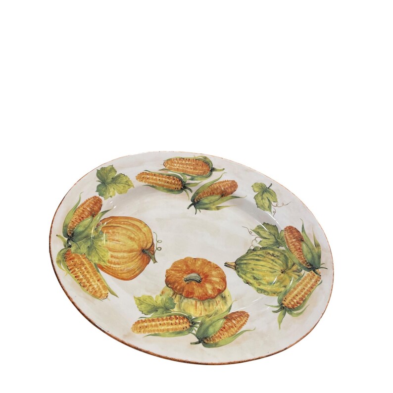 May include: Oval serving platter with a hand-painted design of pumpkins, corn, and green leaves. The platter has a cream-colored background and a brown rim. The artwork features shades of orange, yellow, and green.