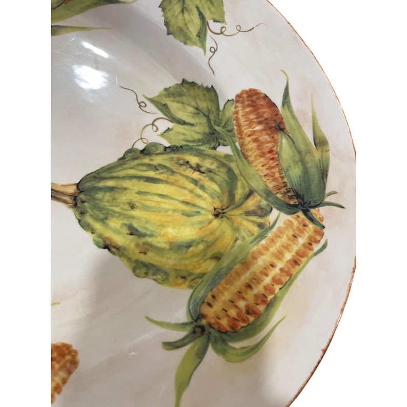 May include: A white ceramic serving dish with a hand-painted design of corn and squash. The corn is a golden yellow with green husks, and the squash is green and yellow. The rim of the dish has a distressed, aged look.