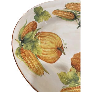 May include: A white ceramic serving platter with a painted harvest design. The design features a large orange pumpkin, ears of corn, and green leaves. The rim of the platter has a brown border.