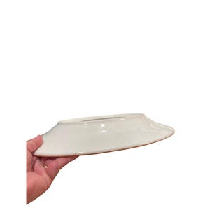 May include: A white ceramic plate with a slightly raised rim and a brown edge. The plate is held by a hand, showcasing its clean design and simple elegance. Ideal for serving food.