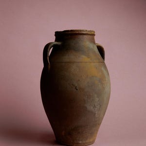 May include: A large, brown, earthenware jug with two handles. The jug has a slightly rounded body and a wide mouth.