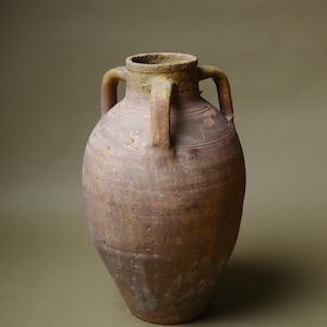 May include: A large, antique terracotta amphora with two handles. The vessel has a bulbous body and a weathered, textured surface with shades of brown and green. This rustic piece is ideal for home decor.