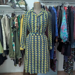 Può includere: Un vestito a motivi gialli e blu con una cintura. Il vestito è su un manichino ed è esposto in un negozio di abbigliamento.