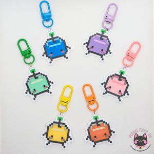 May include: Six pixel art character keychains in blue, purple, green, pink, yellow, and orange. Each keychain features a square-shaped character with a small stem on top and a matching coloured plastic lobster clasp attached to a metal ring.