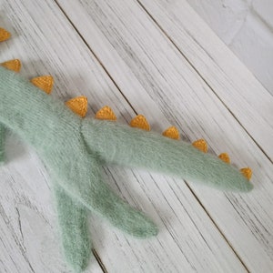 May include: A soft, green knitted dinosaur toy with yellow spikes along its tail.