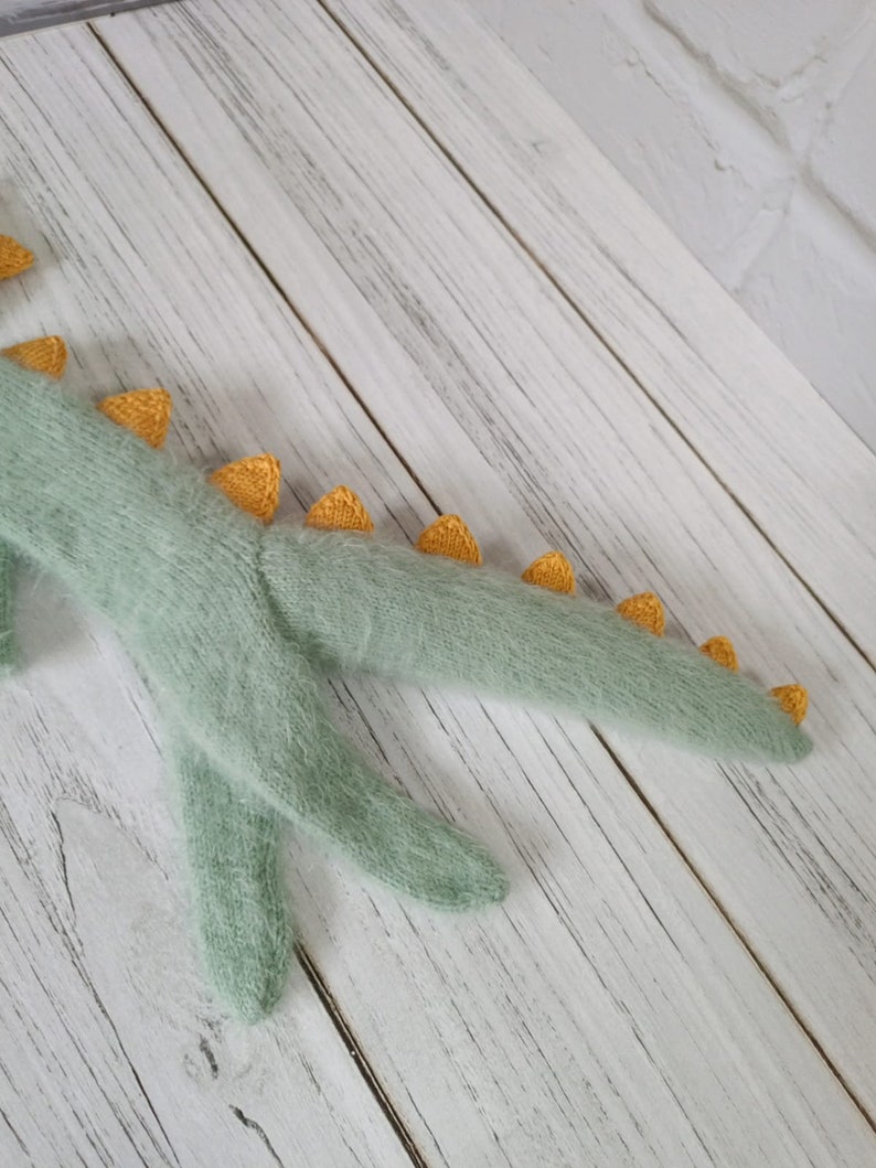 May include: A soft, green knitted dinosaur toy with yellow spikes along its tail.
