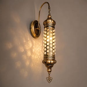 May include: An antique-style wall sconce with a brass finish. The lamp features a cylindrical body with a honeycomb pattern of clear crystals, a decorative top and bottom, and a curved arm. The sconce is mounted on a round brass base.