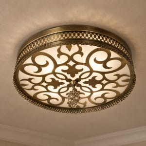 May include: A round flush mount ceiling light fixture with an antique brass finish frame. The metal frame features an intricate cut-out scrollwork pattern over a white diffuser, with a decorative filigree pendant hanging from the center.