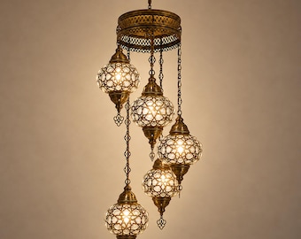 May include: A multi-light pendant chandelier featuring five glowing glass globes suspended from a circular antique brass frame. Each globe is encased in a decorative metal lattice with intricate cutouts, emitting a warm light.