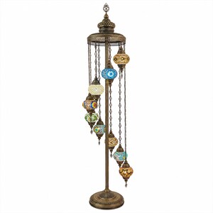 May include: A bronze-colored floor lamp with a decorative design. The lamp features multiple colorful mosaic glass globes hanging from chains. The globes are in various colors, including blue, yellow, and orange. The lamp has a round base and a detailed top.
