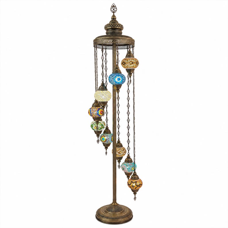 May include: A bronze-colored floor lamp with a decorative design. The lamp features multiple colorful mosaic glass globes hanging from chains. The globes are in various colors, including blue, yellow, and orange. The lamp has a round base and a detailed top.