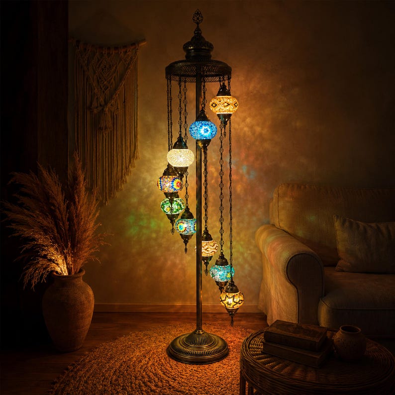 May include: A tall, ornate floor lamp with a dark metal frame and multiple colorful mosaic glass globes. The lamp has a spiral design with the globes hanging at different levels. The base is round and the lamp is lit, casting warm light.