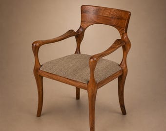 Puede incluir: Un sillón de madera con respaldo curvo, apoyabrazos de líneas fluidas y cuatro patas cónicas. El asiento está tapizado en una tela texturizada de color marrón claro. La madera muestra un veteado natural con un acabado cálido en marrón medio.
