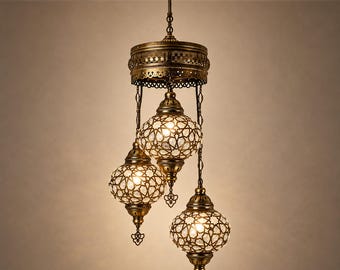 May include: A three-light pendant chandelier featuring antique brass metalwork with intricate filigree patterns. Three spherical glass globes with a white geometric star-shaped overlay hang from a central circular canopy by chains.