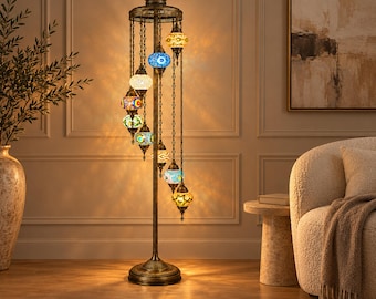 May include: A tall floor lamp with a dark bronze metal stand and nine hanging mosaic glass globes in various colors including blue, yellow, green, and white. The lamp features an ornate top finial and a circular base, emitting a warm glow.