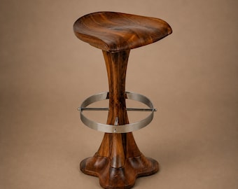 May include: A tall bar stool crafted from dark brown wood with a contoured, saddle-shaped seat. The central pedestal base flares outward at the bottom and features a circular, brushed metal footrest ring secured by horizontal metal supports.