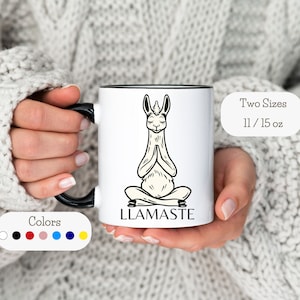 Op de afbeelding: Een witte keramische mok met een zwarte rand en handvat. De mok heeft een zwart-witte illustratie van een lama in een yogapose met de tekst "LLAMASTE". De mok is verkrijgbaar in twee maten: 11 oz en 15 oz.