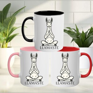 May include: Three white ceramic mugs with black handles. Each mug has a black rim and a different colored interior: pink, red, and black. Each mug features a black and white illustration of a llama in a yoga pose with the text "LLAMASTE" printed below.
