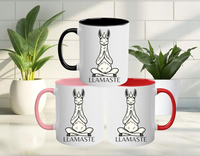 May include: Three white ceramic mugs with black handles. Each mug has a black rim and a different colored interior: pink, red, and black. Each mug features a black and white illustration of a llama in a yoga pose with the text "LLAMASTE" printed below.