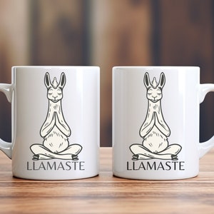 May include: Two white ceramic mugs with black illustrations of llamas in a yoga pose. The text "LLAMASTE" is printed on the bottom of each mug.