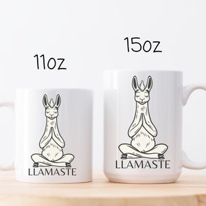 May include: Two white ceramic mugs with a black and white illustration of a llama in a yoga pose. The text "LLAMASTE" is printed on the mugs. The mugs are 11 oz and 15 oz.
