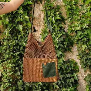 May include: A brown and green crocheted tote bag with a smaller green crocheted pocket on the front. The bag is hanging from a green crocheted strap.